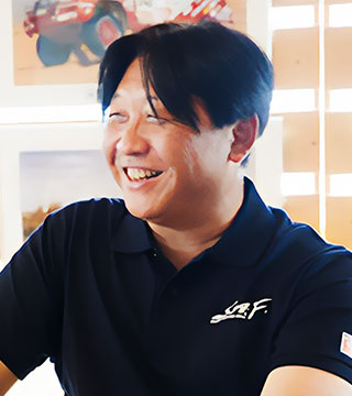 さなげアドベンチャーフィールドの黒いポロシャツを着て、笑顔の藤岡さん